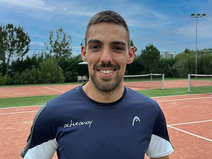 Smiling tennis coach on a clay court, wearing an Active Away shirt.