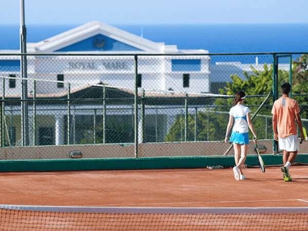 Two players walking off a clay tennis court at a seaside resort, holding racquets.
