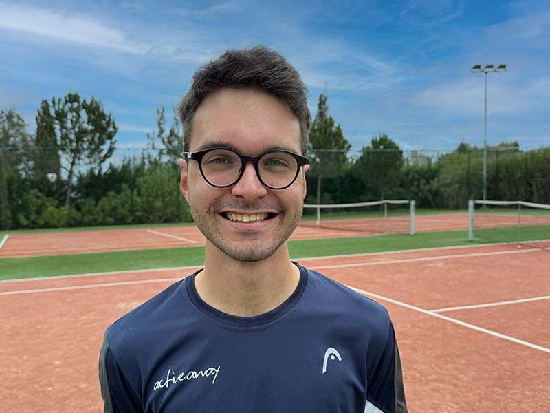 Smiling tennis coach in glasses on a clay court at Ikos Odisia resort.