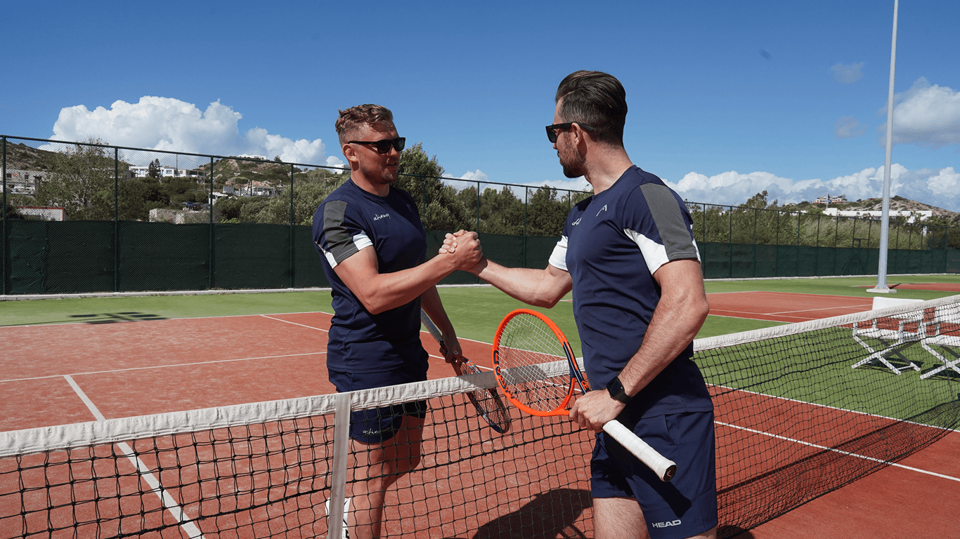 Two tennis players shake hands at the net on a sunny court.