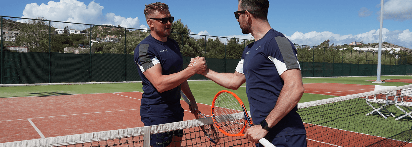 Two tennis players shake hands at the net on a sunny court.