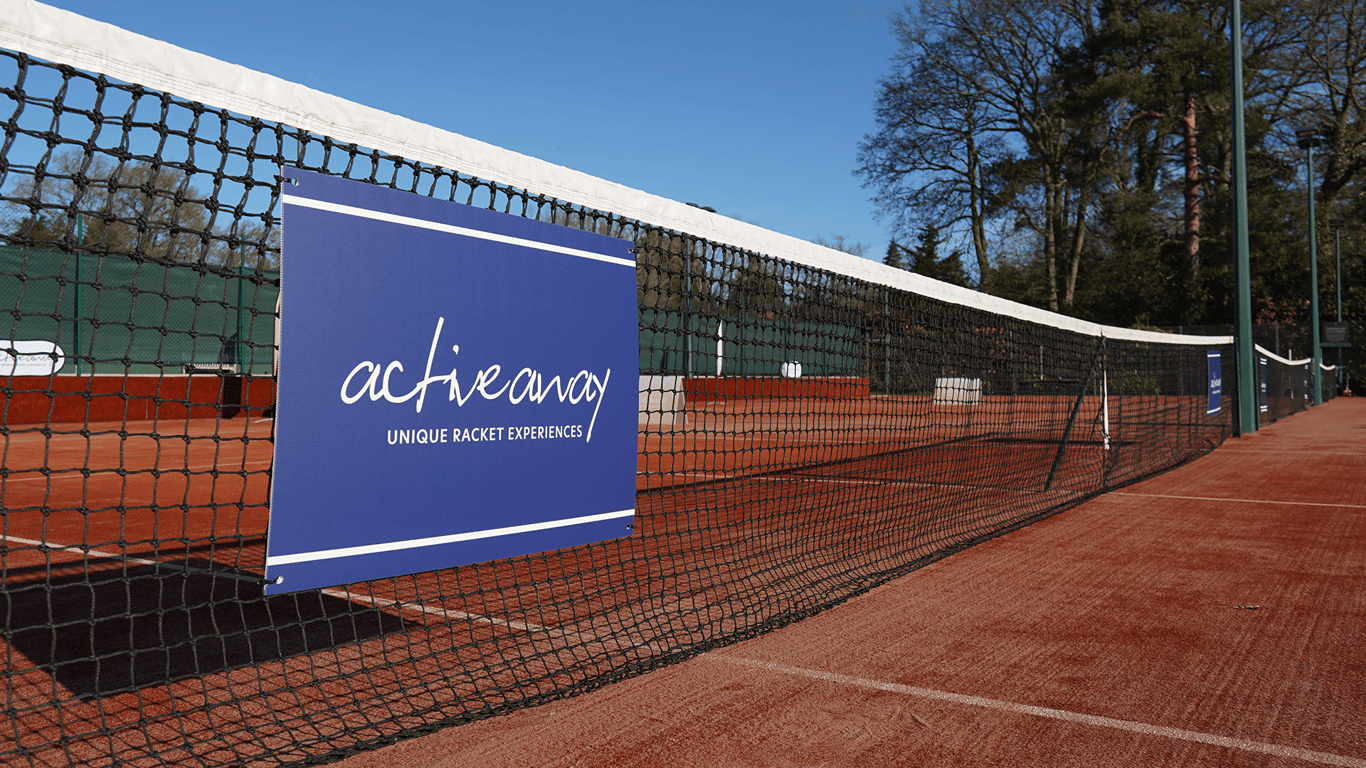 Clay tennis court with a net-mounted Active Away sign on a sunny day.