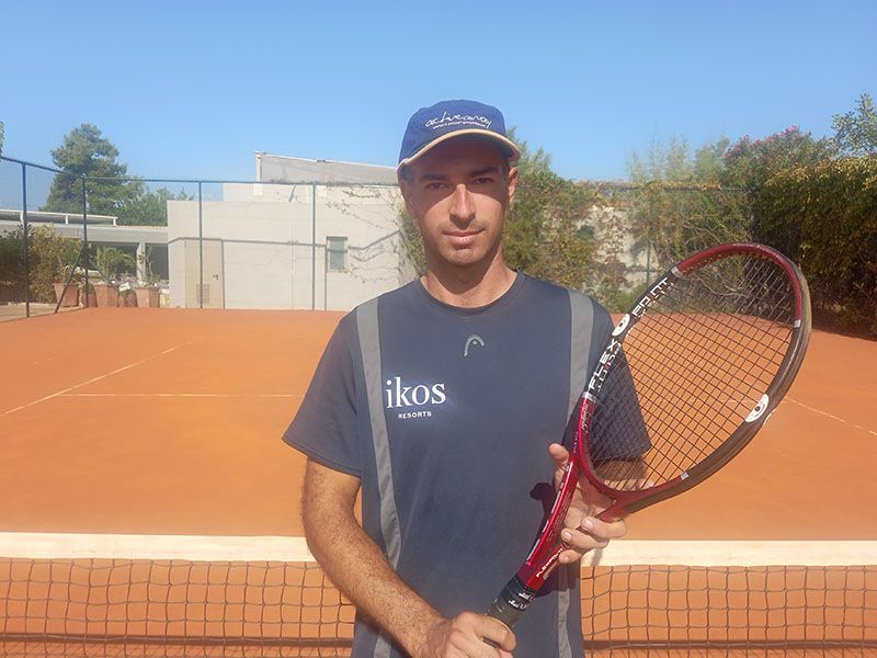 Tennis coach holding a racket on a clay court at Ikos Olivia resort.