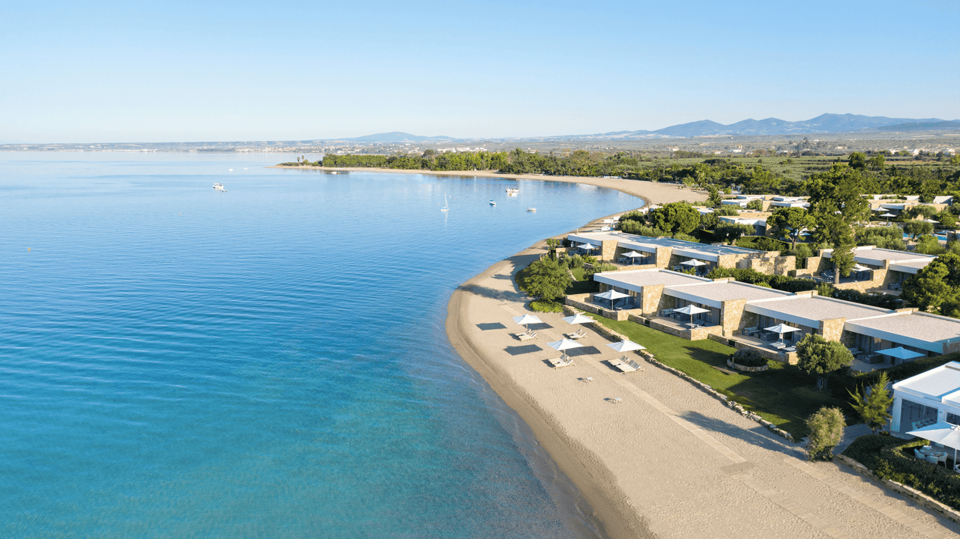 Aerial view of Ikos Resorts: beachfront villas, sandy bay, calm blue sea and sun loungers.