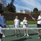 Coach demonstrates forehand to junior players during a school tennis clinic on an outdoor court.