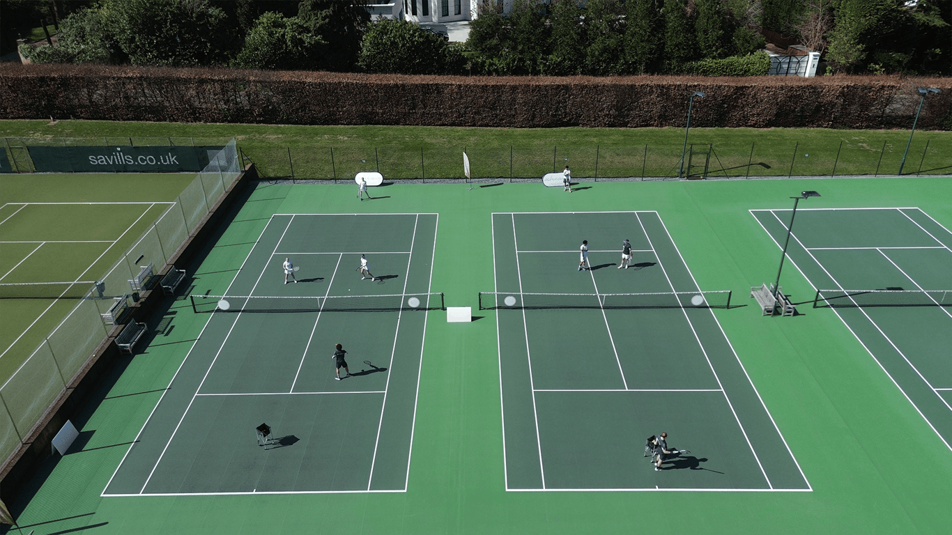 Aerial view of multiple green tennis courts with players practising in small groups.