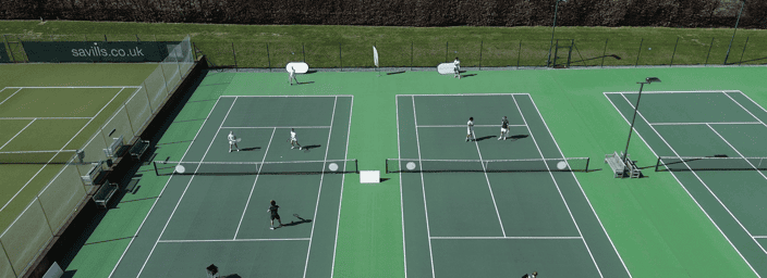 Aerial view of multiple green tennis courts with players practising in small groups.