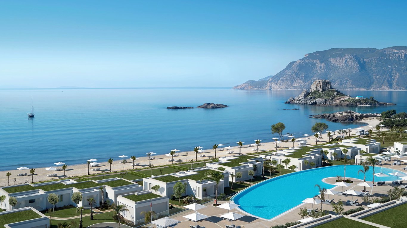 Ikos Aria beachfront resort with infinity pool, white villas, and calm Aegean sea with rocky islet.