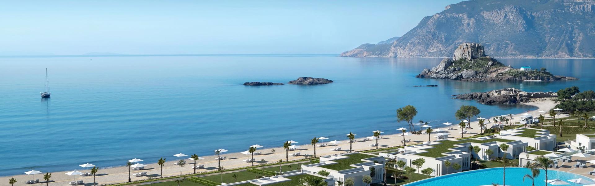 Ikos Aria beachfront resort with infinity pool, white villas, and calm Aegean sea with rocky islet.