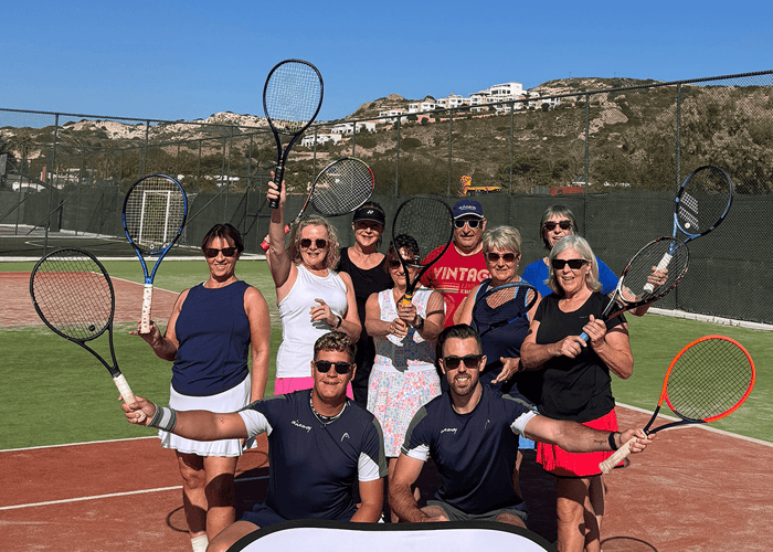 Group of adults posing with tennis rackets on court with Active Away sign.