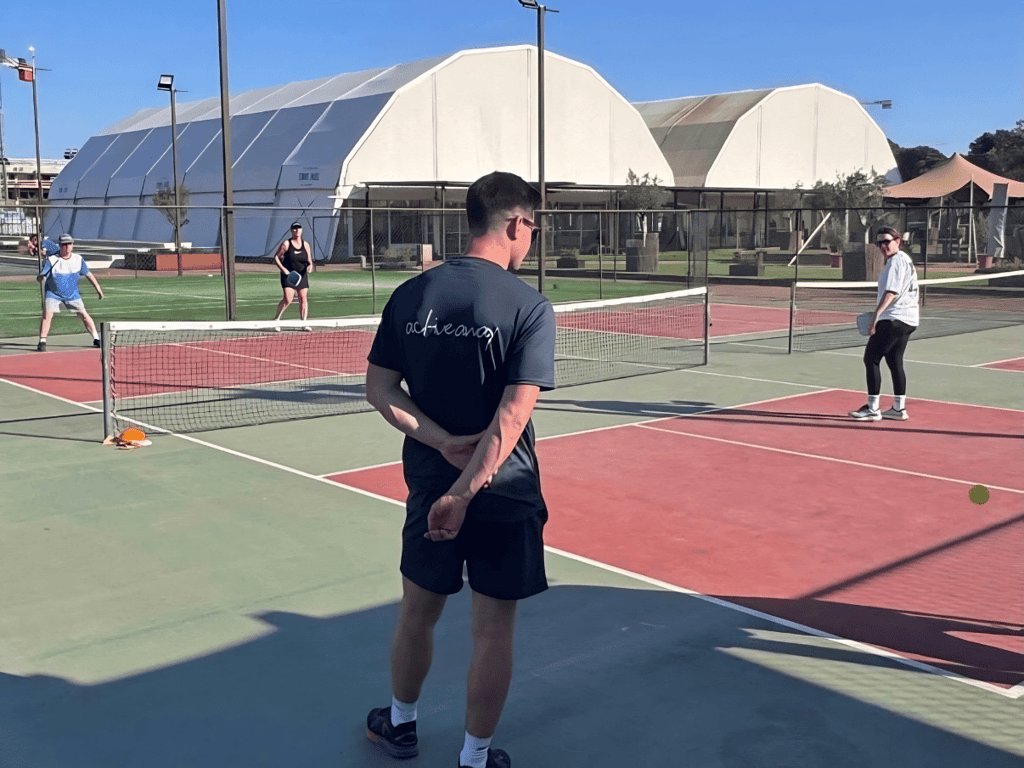 Coach observes players during an outdoor pickleball clinic on sunny courts.