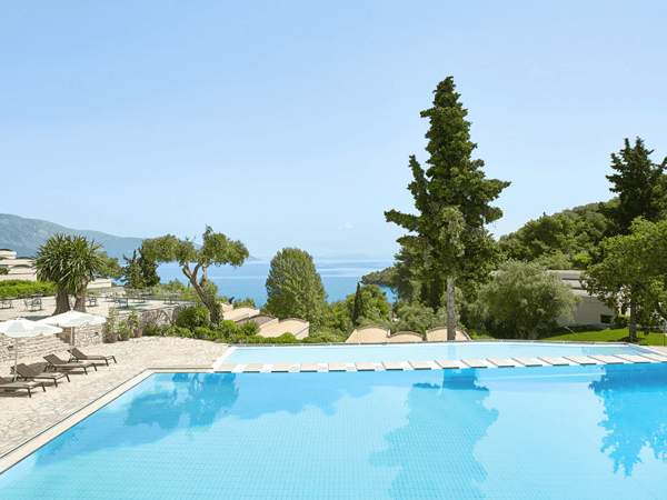 Hillside infinity pool with sun loungers, trees and blue sea views at a Mediterranean resort.