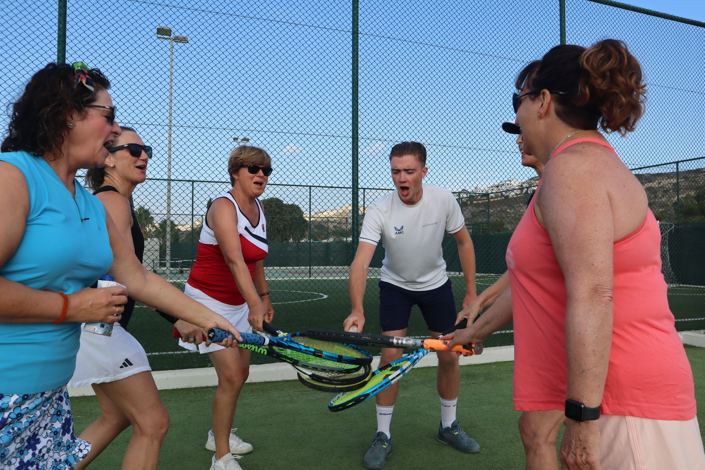 Active Away guests and their coach stack their rackets together in a team huddle beside the court